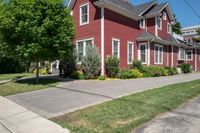 a large brick house with white windows next to a sidewalk and green trees on either side of the street