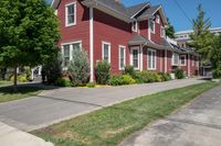 a large brick house with white windows next to a sidewalk and green trees on either side of the street