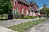 a large brick house with white windows next to a sidewalk and green trees on either side of the street