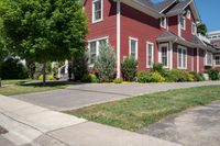 a large brick house with white windows next to a sidewalk and green trees on either side of the street