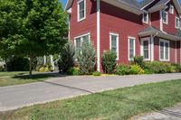 a large brick house with white windows next to a sidewalk and green trees on either side of the street