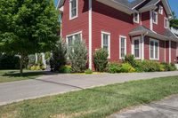 a large brick house with white windows next to a sidewalk and green trees on either side of the street