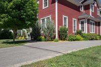 a large brick house with white windows next to a sidewalk and green trees on either side of the street