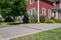 a large brick house with white windows next to a sidewalk and green trees on either side of the street