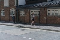 man in hat with black jacket and blue coat walking down side walk near brick building