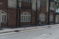 man in hat with black jacket and blue coat walking down side walk near brick building