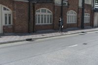 man in hat with black jacket and blue coat walking down side walk near brick building