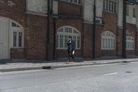 man in hat with black jacket and blue coat walking down side walk near brick building