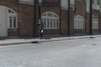 man in hat with black jacket and blue coat walking down side walk near brick building
