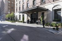 three people in suits standing outside the entrance to a large hotel or apartment building with an awning