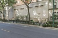 an empty street in front of an old white house with trees and bushes in front