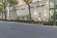 an empty street in front of an old white house with trees and bushes in front