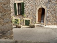 the building is made of stones and stone walls and two chairs and one potted planter