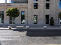 a building with two large round marble planters on the sidewalk next to a tree