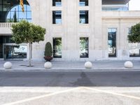 a building with two large round marble planters on the sidewalk next to a tree