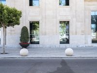 a building with two large round marble planters on the sidewalk next to a tree