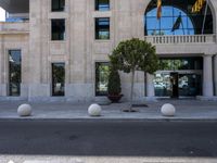 a building with two large round marble planters on the sidewalk next to a tree