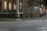 a crosswalk at night near a busy city street with buildings and a no parking sign