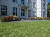 a beautiful lawn with flowers near a large white house with two chimneys and a balcony