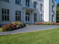 a beautiful lawn with flowers near a large white house with two chimneys and a balcony