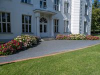 a beautiful lawn with flowers near a large white house with two chimneys and a balcony