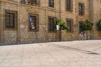 a man walks down a paved street past stone buildings and orange trees that sit on either side