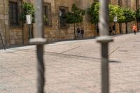 a man walks down a paved street past stone buildings and orange trees that sit on either side