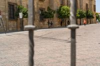 a man walks down a paved street past stone buildings and orange trees that sit on either side