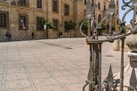 a man walks down a paved street past stone buildings and orange trees that sit on either side