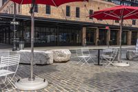 tables and umbrellas outside on brick sidewalk with buildings in background and cobblestone