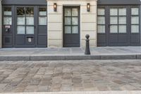 a building with two doors and a parking meter on a cobblestone street next to it