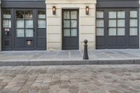 a building with two doors and a parking meter on a cobblestone street next to it