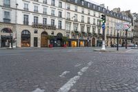 an empty cobbled street with several stores along the sidewalk on both sides and three story buildings in the background