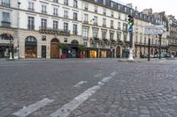 an empty cobbled street with several stores along the sidewalk on both sides and three story buildings in the background