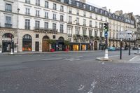 an empty cobbled street with several stores along the sidewalk on both sides and three story buildings in the background