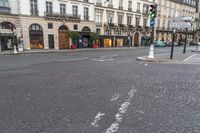 an empty cobbled street with several stores along the sidewalk on both sides and three story buildings in the background