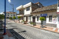 there is a small restaurant with people walking on the side walk that has white buildings in the background