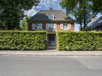 a very cute house in the middle of the road with hedges around it and some windows