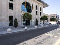 a building next to the street is empty and there are trees around it and shrubs in front are on the street