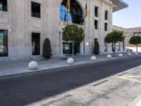 a building next to the street is empty and there are trees around it and shrubs in front are on the street