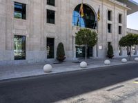 a building next to the street is empty and there are trees around it and shrubs in front are on the street