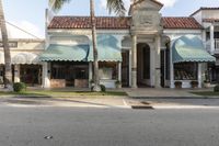 a street is lined with shops and palm trees on either side of it, and some are with large awnings