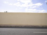 a white wall with a street sign and traffic signal below it, while the sky is blue and white