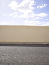 a white wall with a street sign and traffic signal below it, while the sky is blue and white