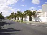 a long street with trees in the middle of it next to a white building and a fence