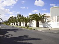 a long street with trees in the middle of it next to a white building and a fence