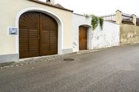 a narrow road leads to a white house and door with a wooden handle and a metal pole on one side