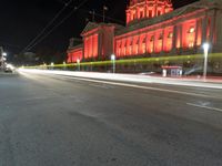 an image of the red light of a building on a street at night in front of it