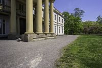 an elegant stone building with two columns and a stone lawn underneath it that has grass growing in the area