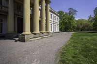 an elegant stone building with two columns and a stone lawn underneath it that has grass growing in the area